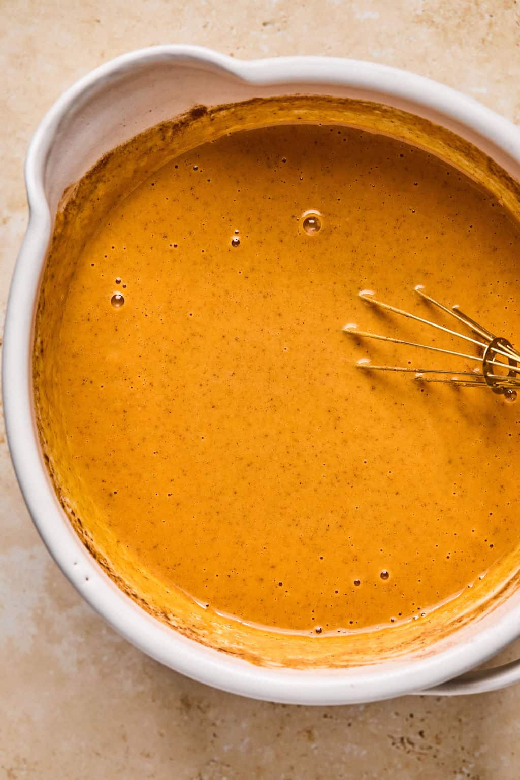 Pumpkin pie mixture in bowl with whisk.
