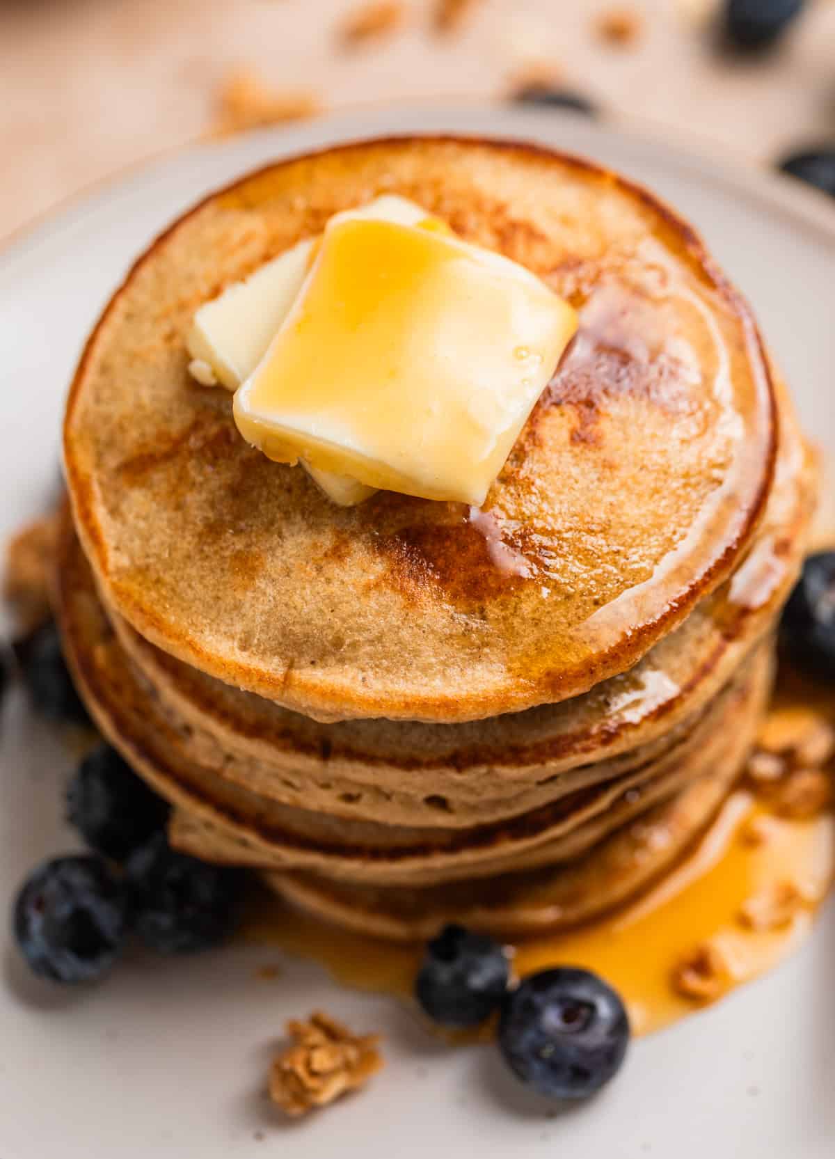 Stack of banana oatmeal blender pancakes on plate with butter and syrup.