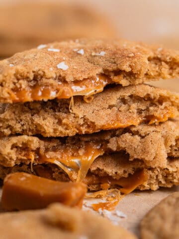 Stack of caramel filled cookies broken in half with caramel oozing out of the centers.