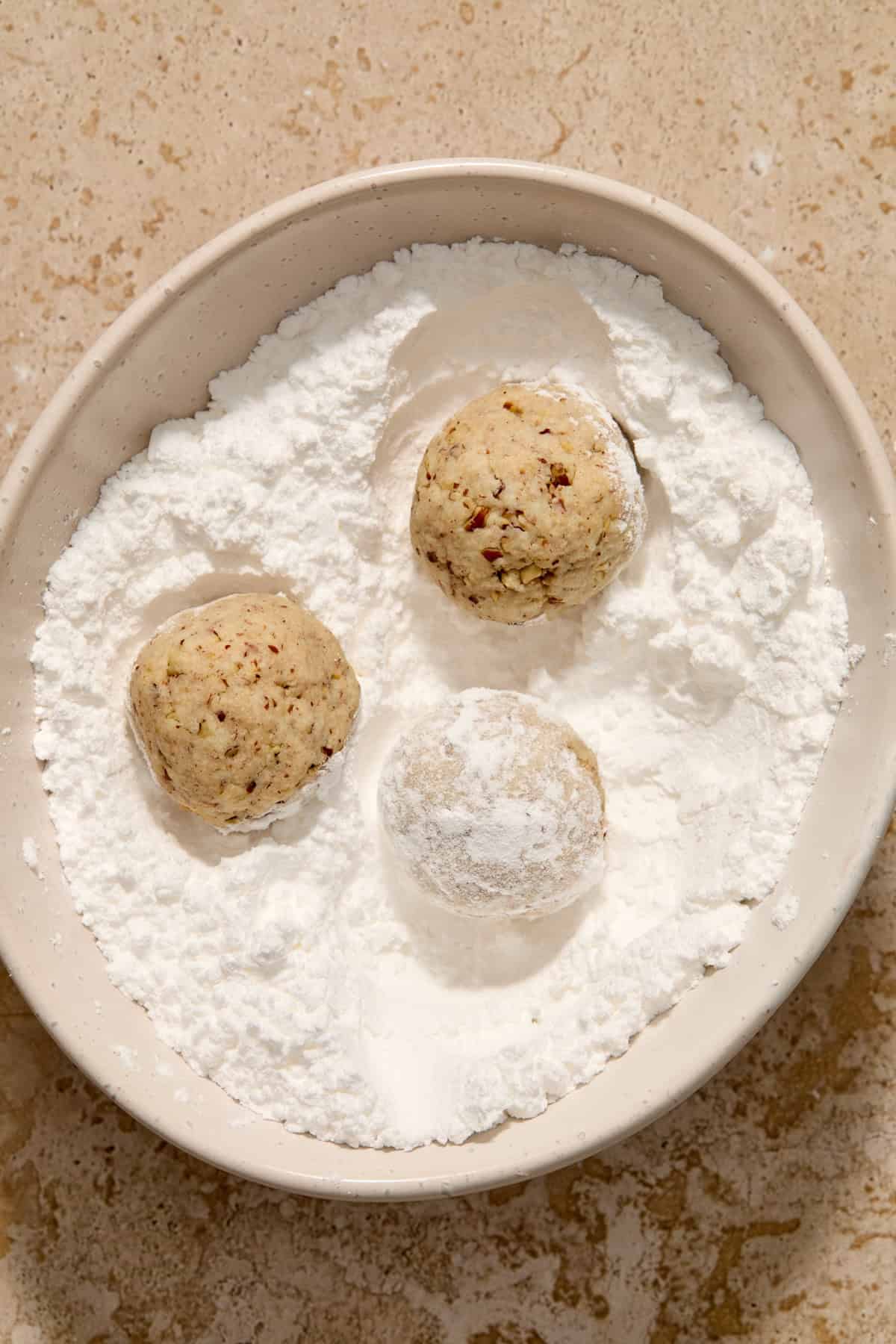 Snowball cookies rolled in powdered sugar in bowl.