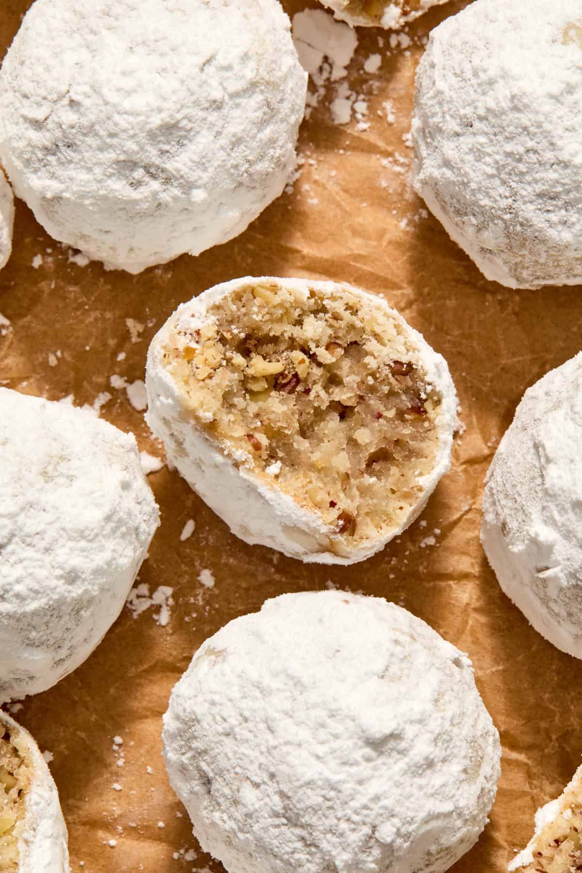 Parchment paper with pecan snowball cookies arranged on top and bite taken from one cookie.