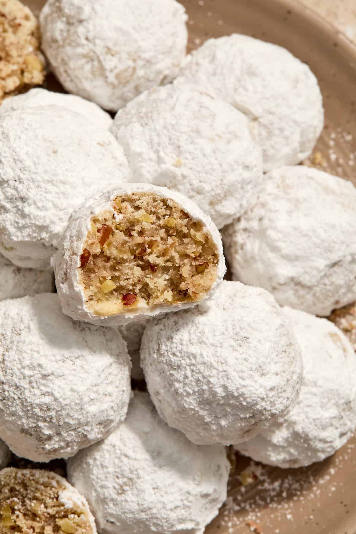 Cream cheese Christmas cookies with pecans and covered in powdered sugar on plate with bite taken out of one cookie.