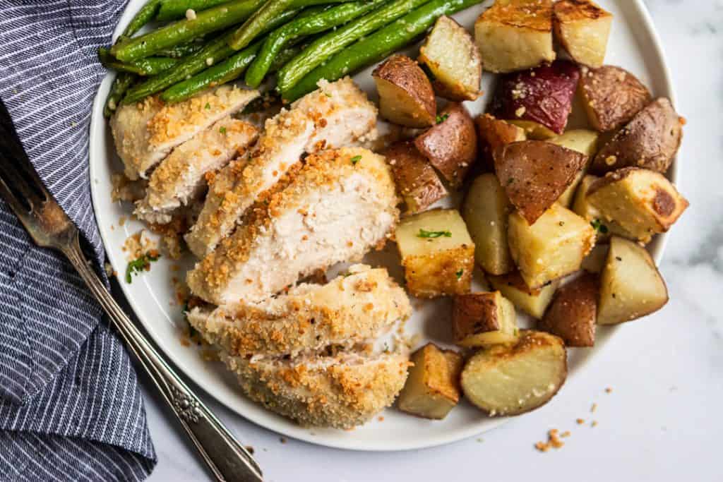 Sliced parmesan chicken with potatoes and green beans.