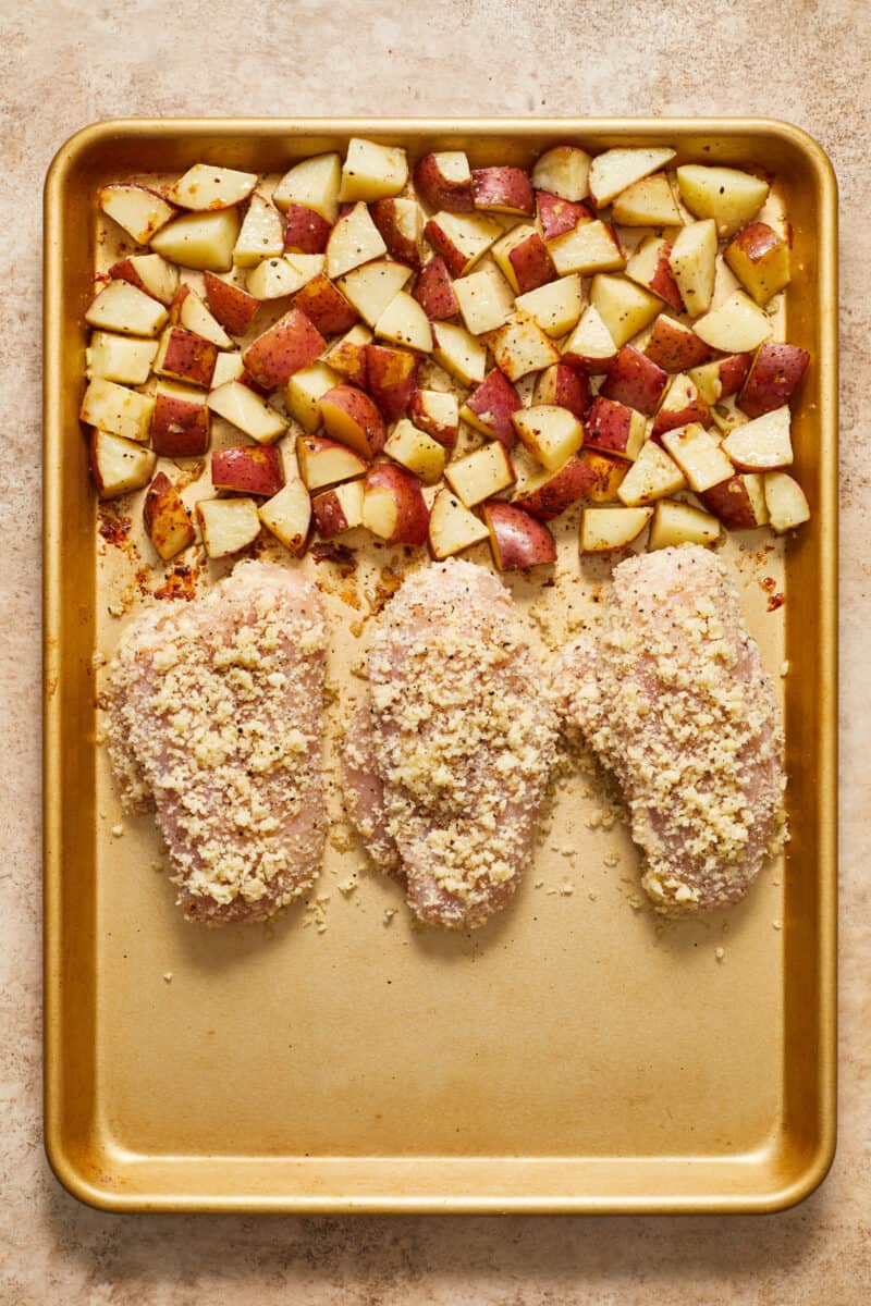 Chicken added to sheet pan with quartered red potatoes.