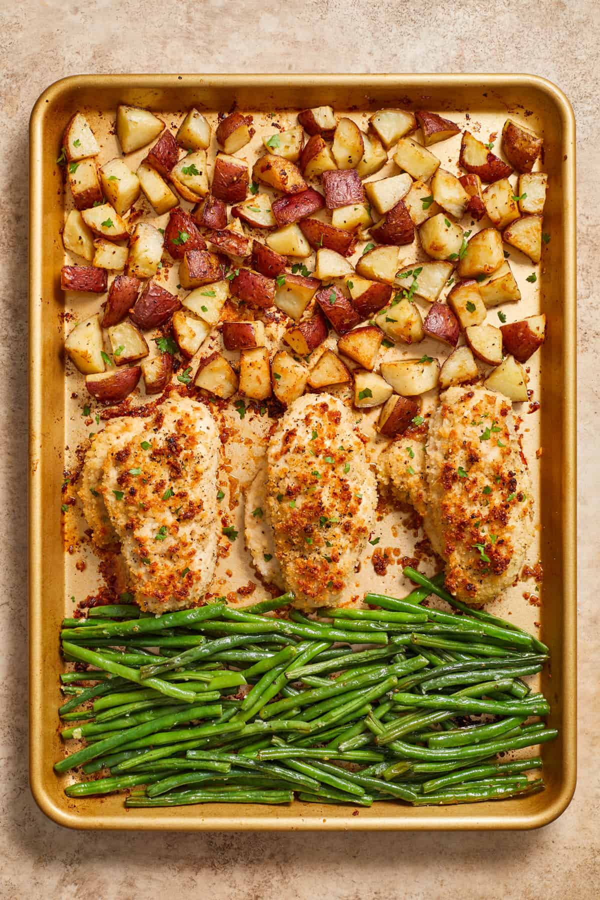 Parmesan sheet pan chicken dinner cooked with potatoes and green beans on gold pan.