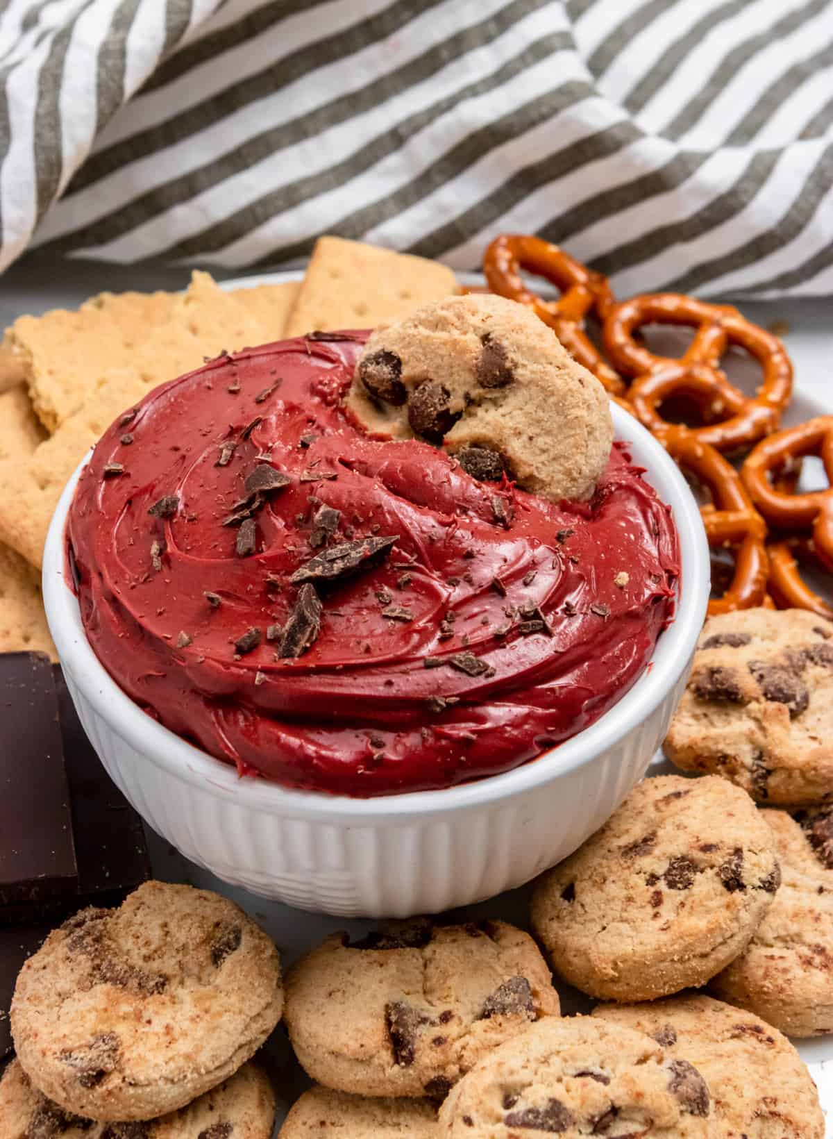 Red velvet cheesecake dip in white bowl with pretzels, cookies etc.