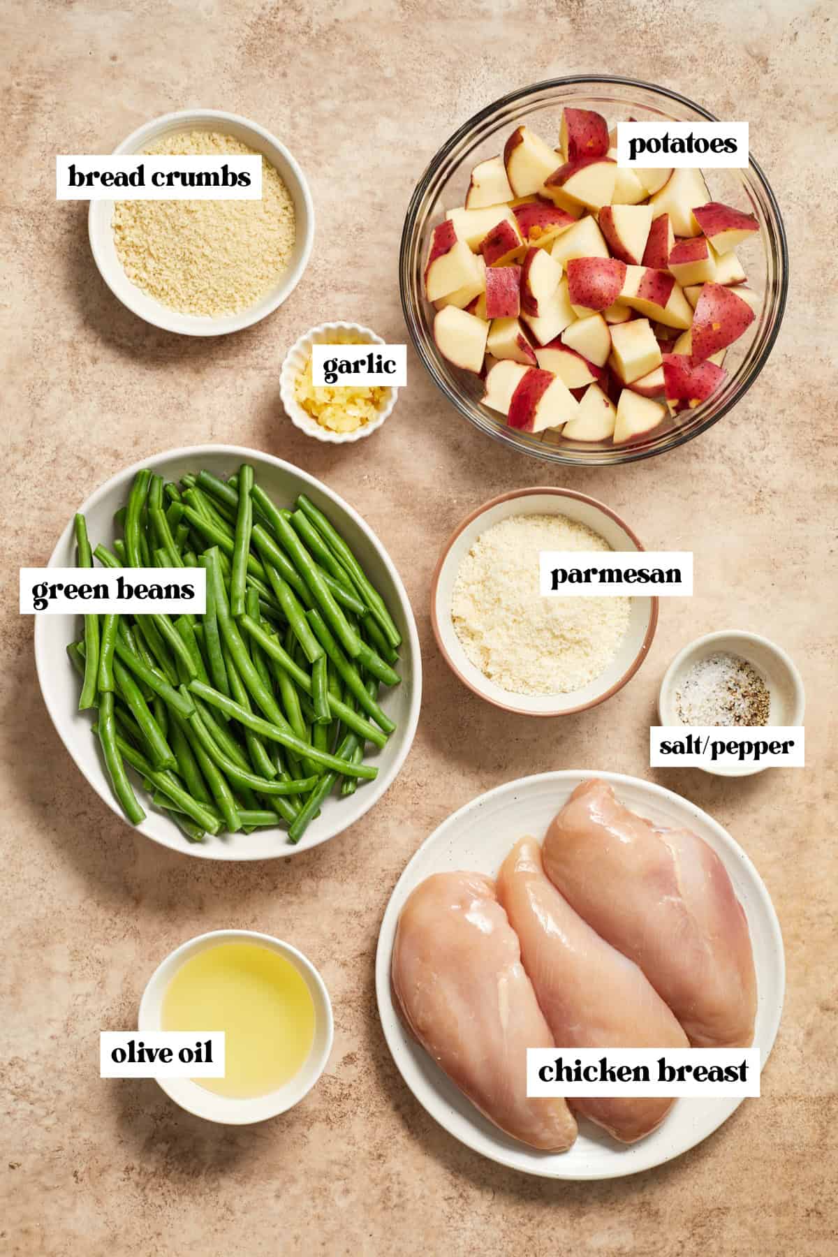Chicken breast, green beans, potatoes, olive oil, parmesan and other labeled ingredients needed for recipe on surface.