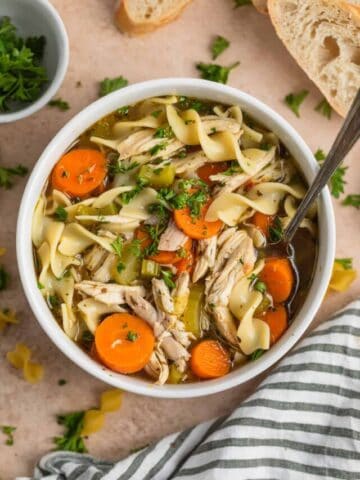 Rotisserie chicken noodle soup in bowl with soup spoon topped with chopped parsley.