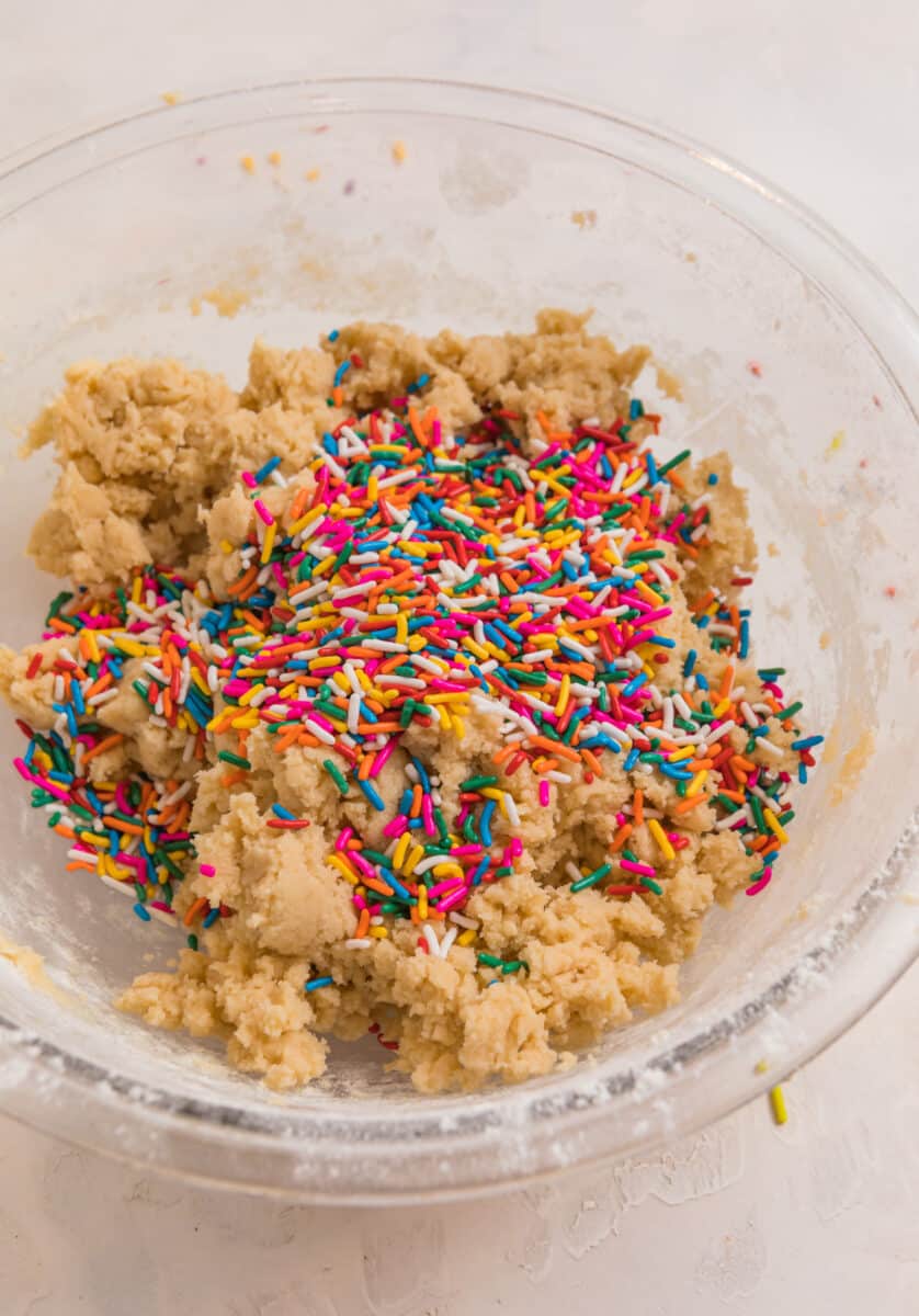 Sprinkles poured over top of birthday cake cookie dough in mixing bowl.