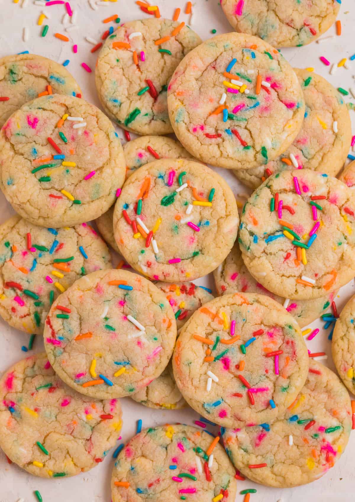 Birthday cake funfetti cookies laying on counter with rainbow sprinkles over top and surrounding.
