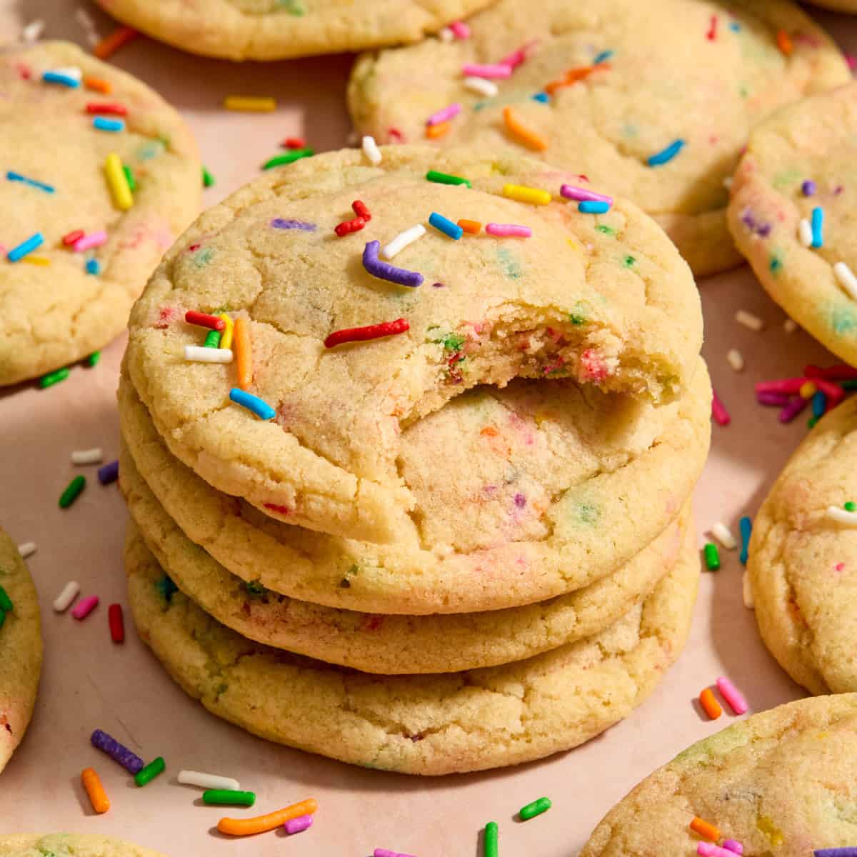 Stack of funfetti rainbow sprinkle filled cookies with bite taken from the cookie on top of stack.