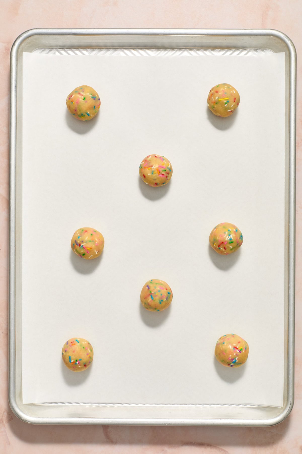 Birthday cake cookie balls on parchment paper lined cookie sheet before baking.