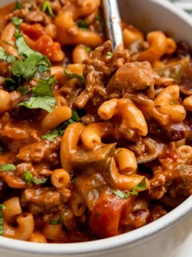 White bowl with chili macaroni and cheese with spoon scooping into it.