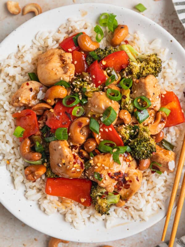 Baked cashew chicken over rice on plate with chopsticks.