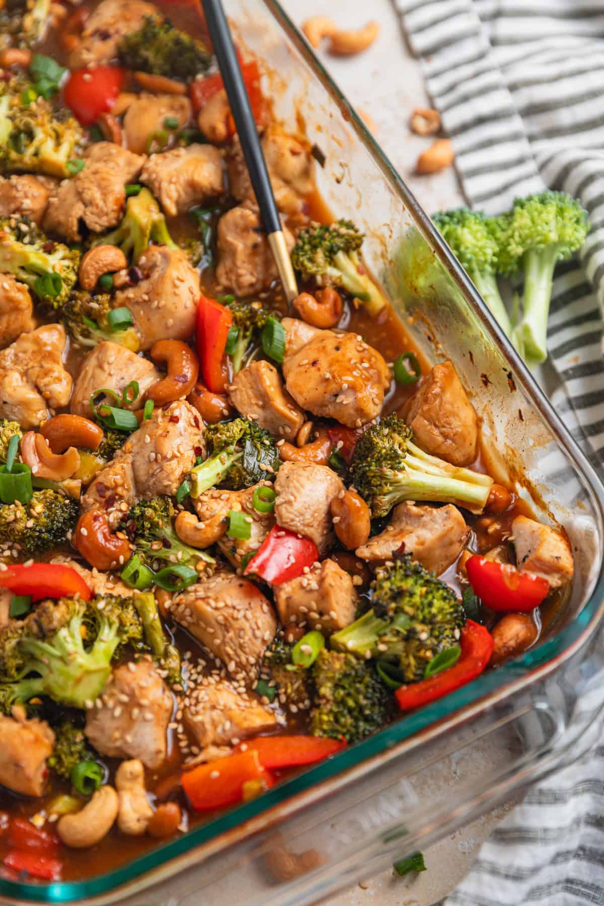 Glass baking pan with easy cashew chicken recipe and spoon scooping into it.