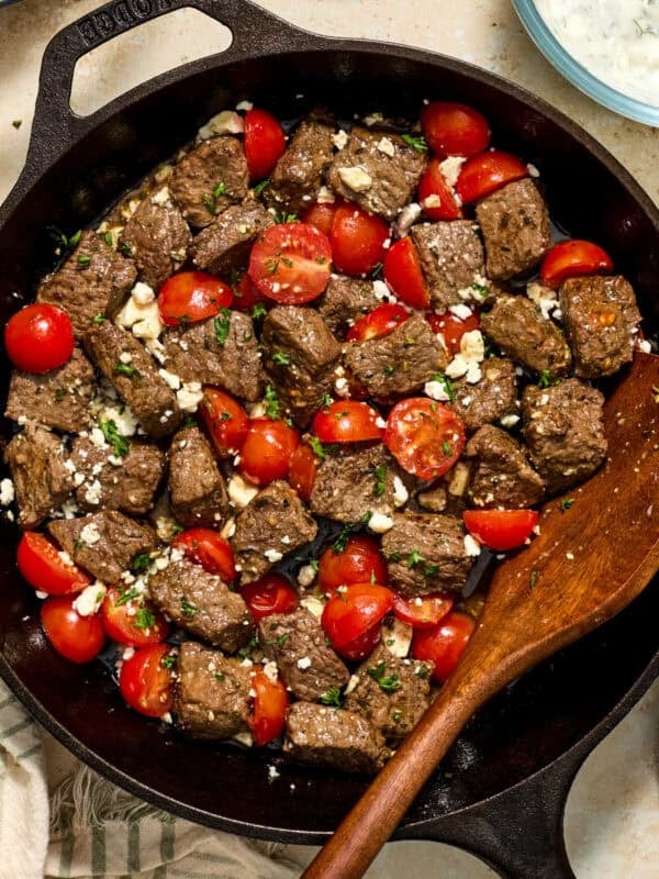Cast iron skillet with steak bites and cherry tomatoes topped with feta cheese.