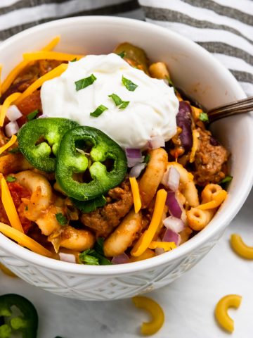 Chili mac and cheese in bowl with sour cream and jalapeno.