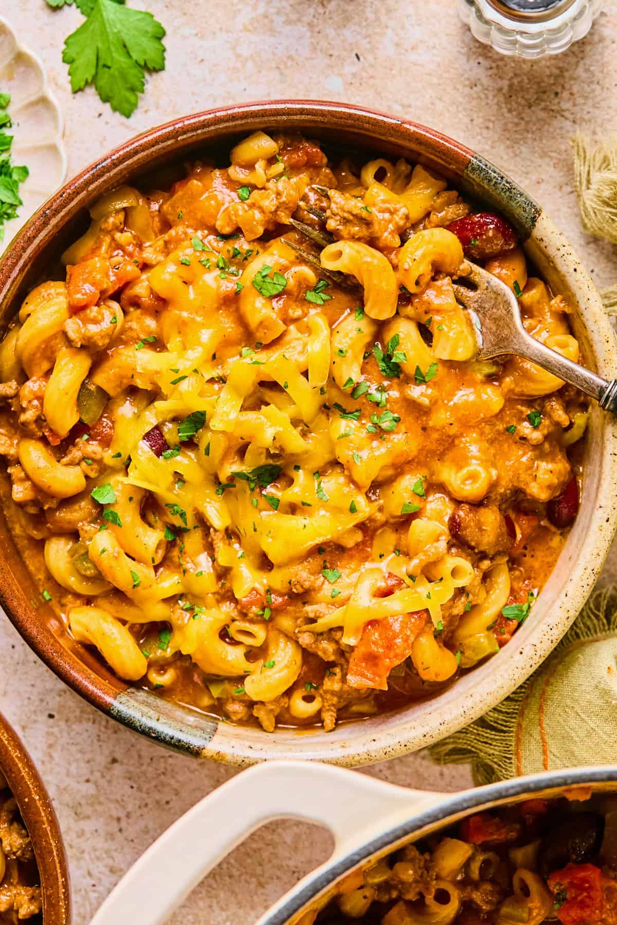 Bowl of chili mac and cheese topped with shredded cheese and parsley.