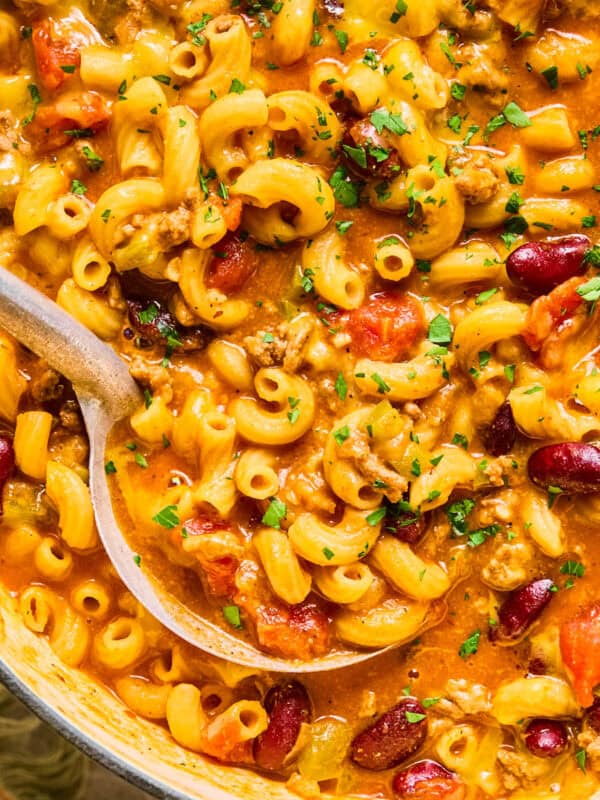 Ladle scooping up chili macaroni and cheese in pot.
