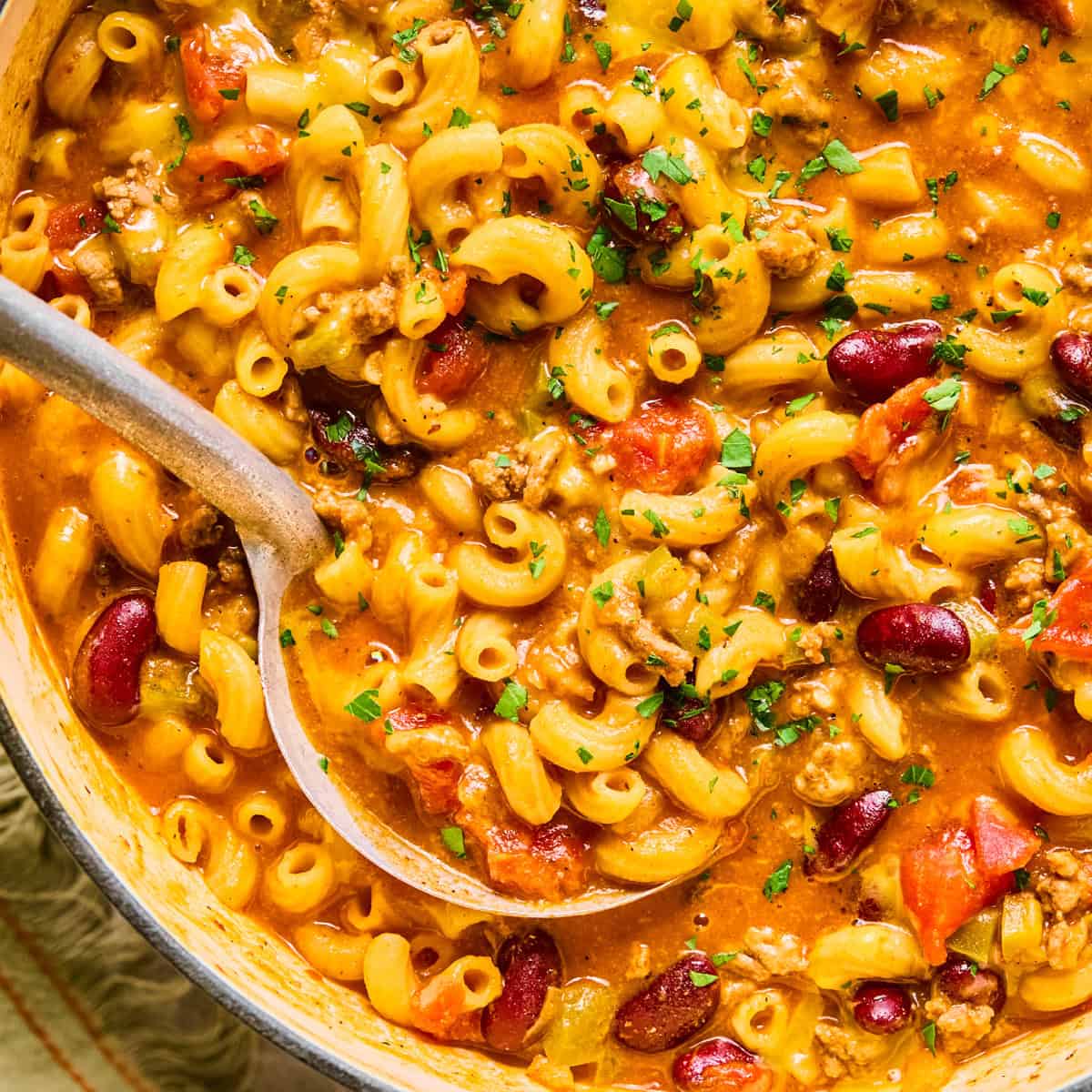 Ladle scooping up chili macaroni and cheese in pot.