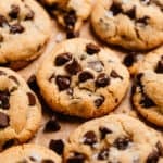 Chocolate chip cookies lined on parchment paper with crumbs and chocolate chips surrounding.