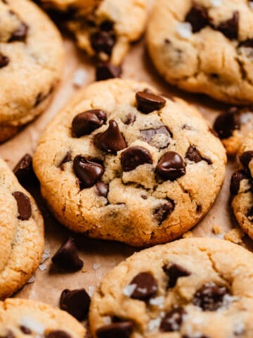 Chocolate chip cookies lined on parchment paper with crumbs and chocolate chips surrounding.