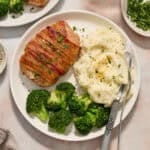 White plate with pork chop dinner including mashed potatoes and broccoli.