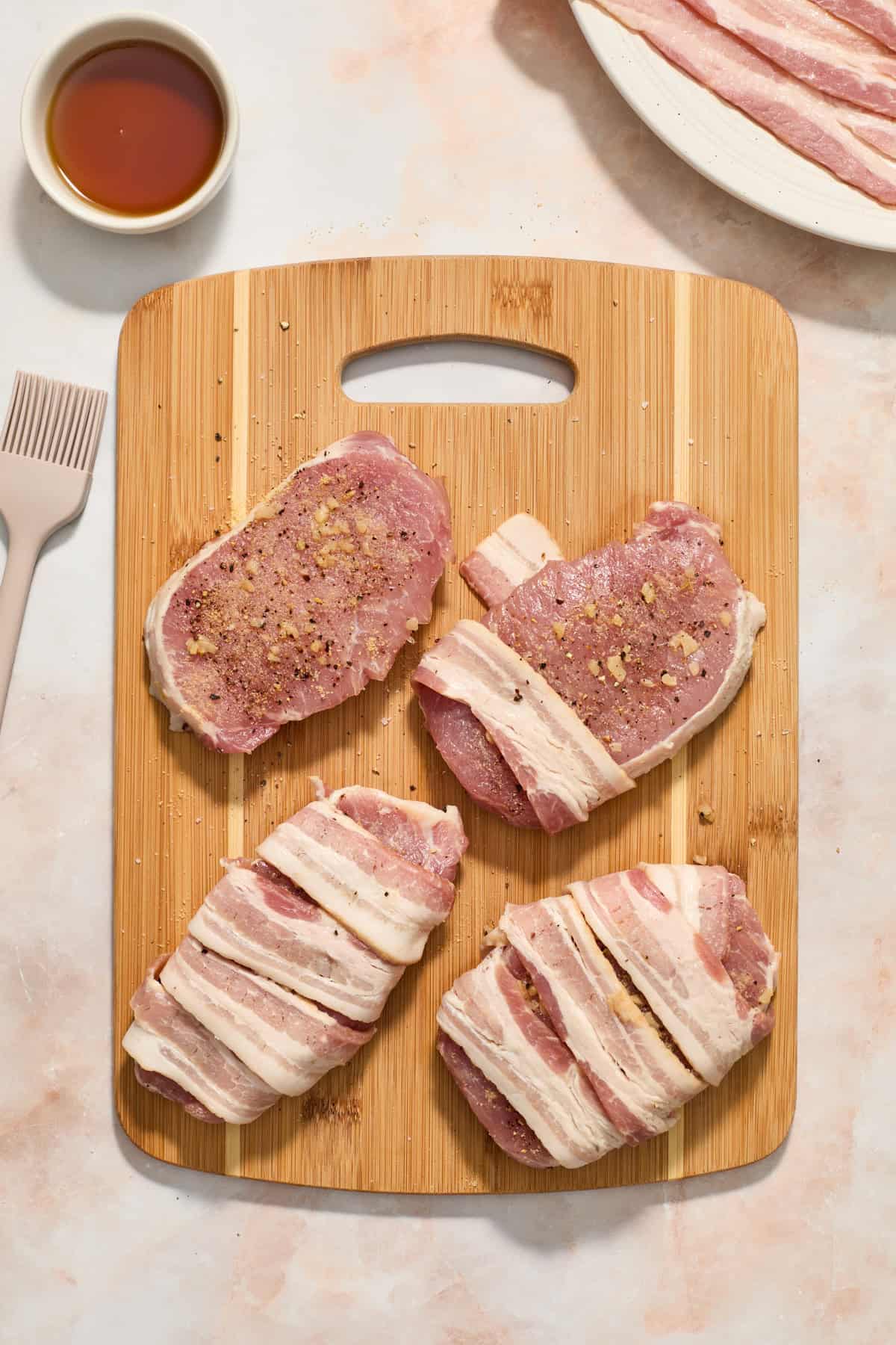 Pork chops with bacon strips wrapped around on cutting board.