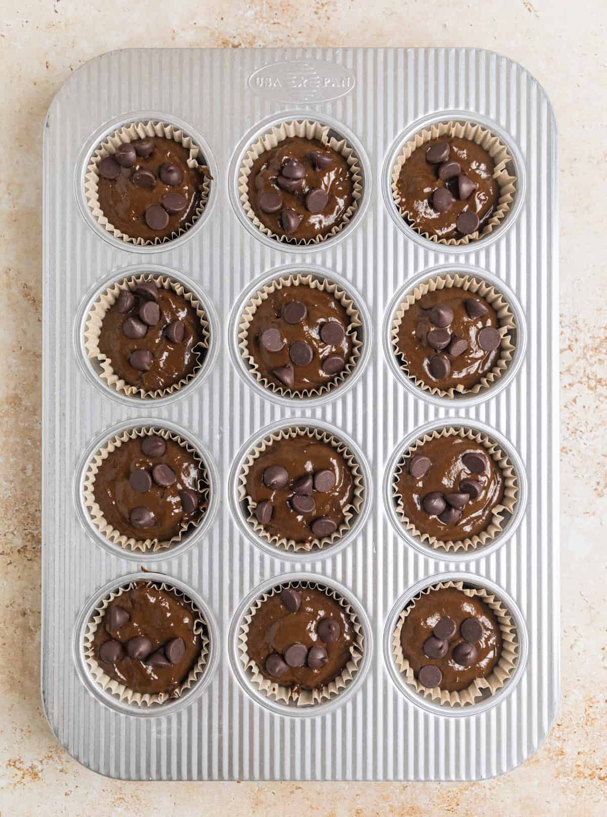 Muffin batter scooped in muffin pan with chocolate chips on top.