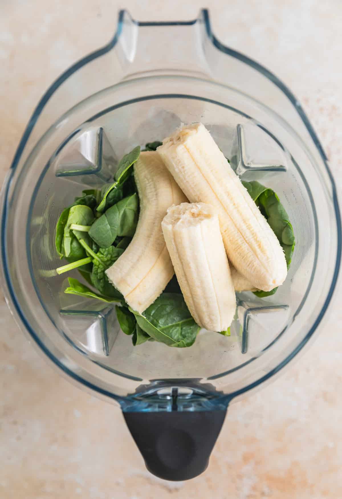 Bananas, milk and spinach in blender before being blended.