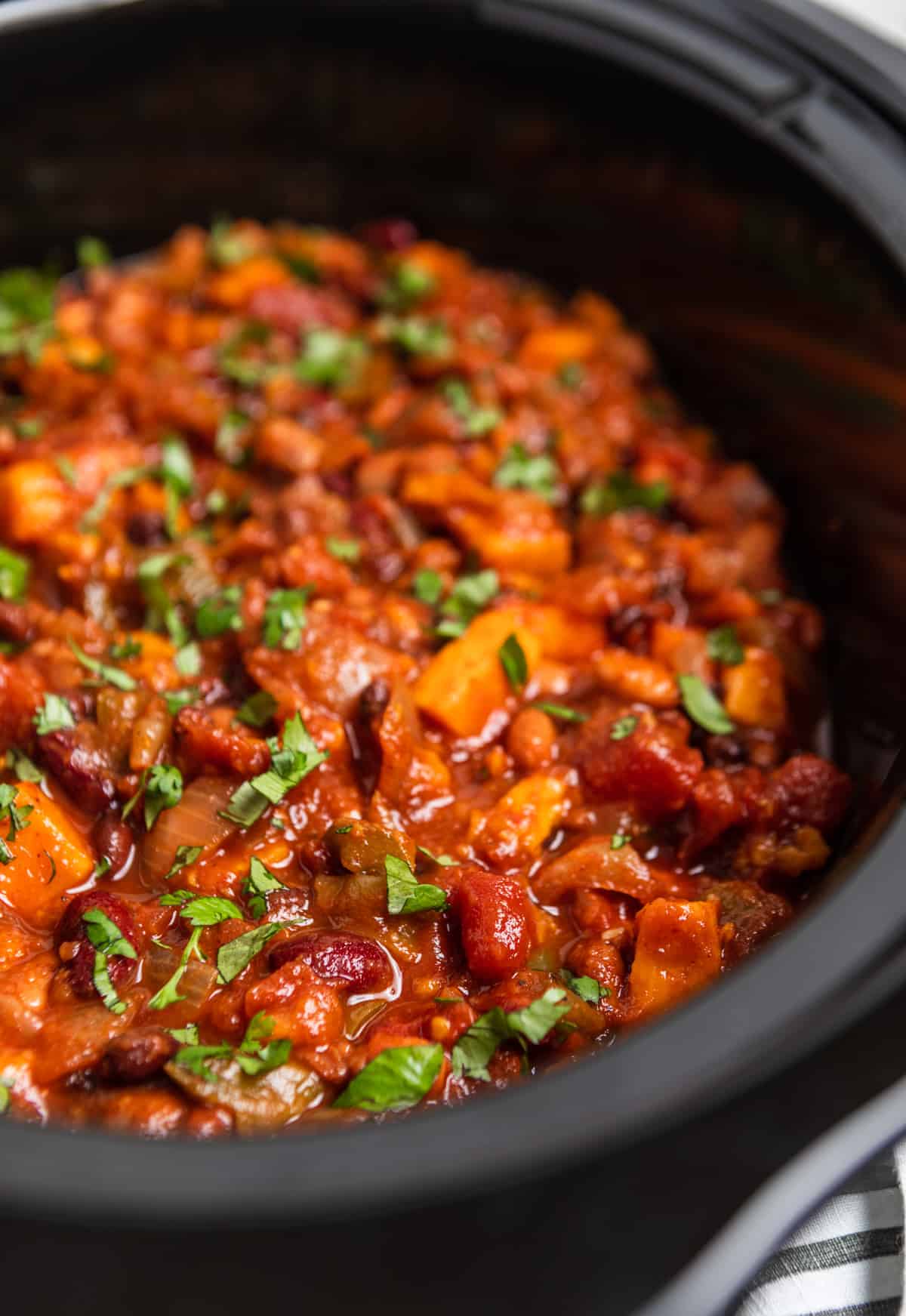 Black slow cooker with cooked sweet potato chili topped with chopped cilantro.
