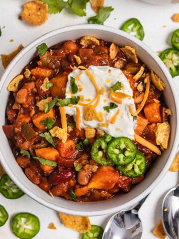 Bowl of sweet potato chili with toppings and spoon beside.