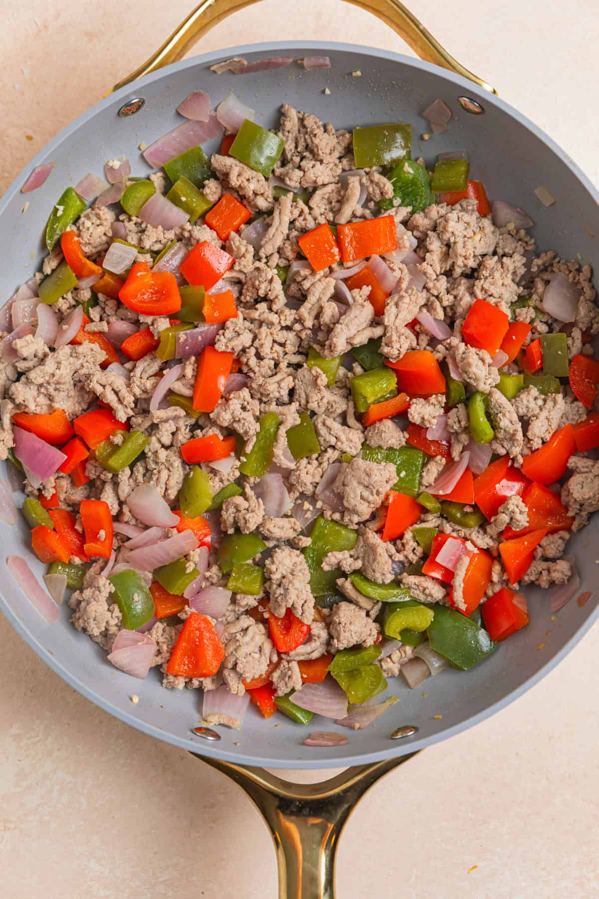 Ground turkey with onions and peppers browned in a skillet.