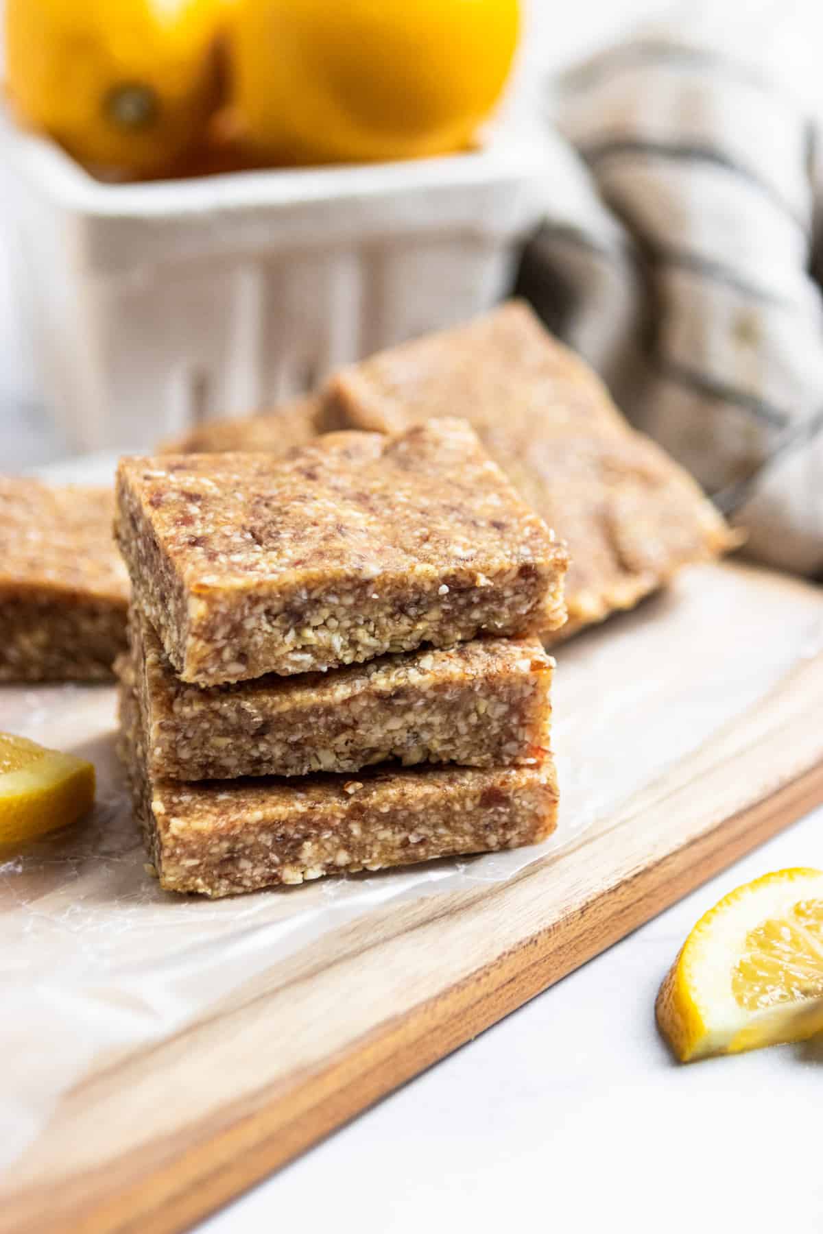 Stack of lemon coconut bars on cutting board with fresh lemons.