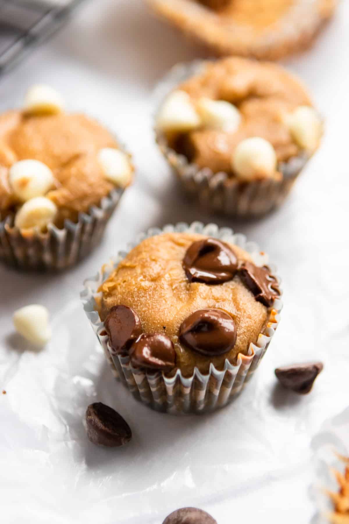 Mini muffins with chocolate chips melted on top laying on top of parchment.