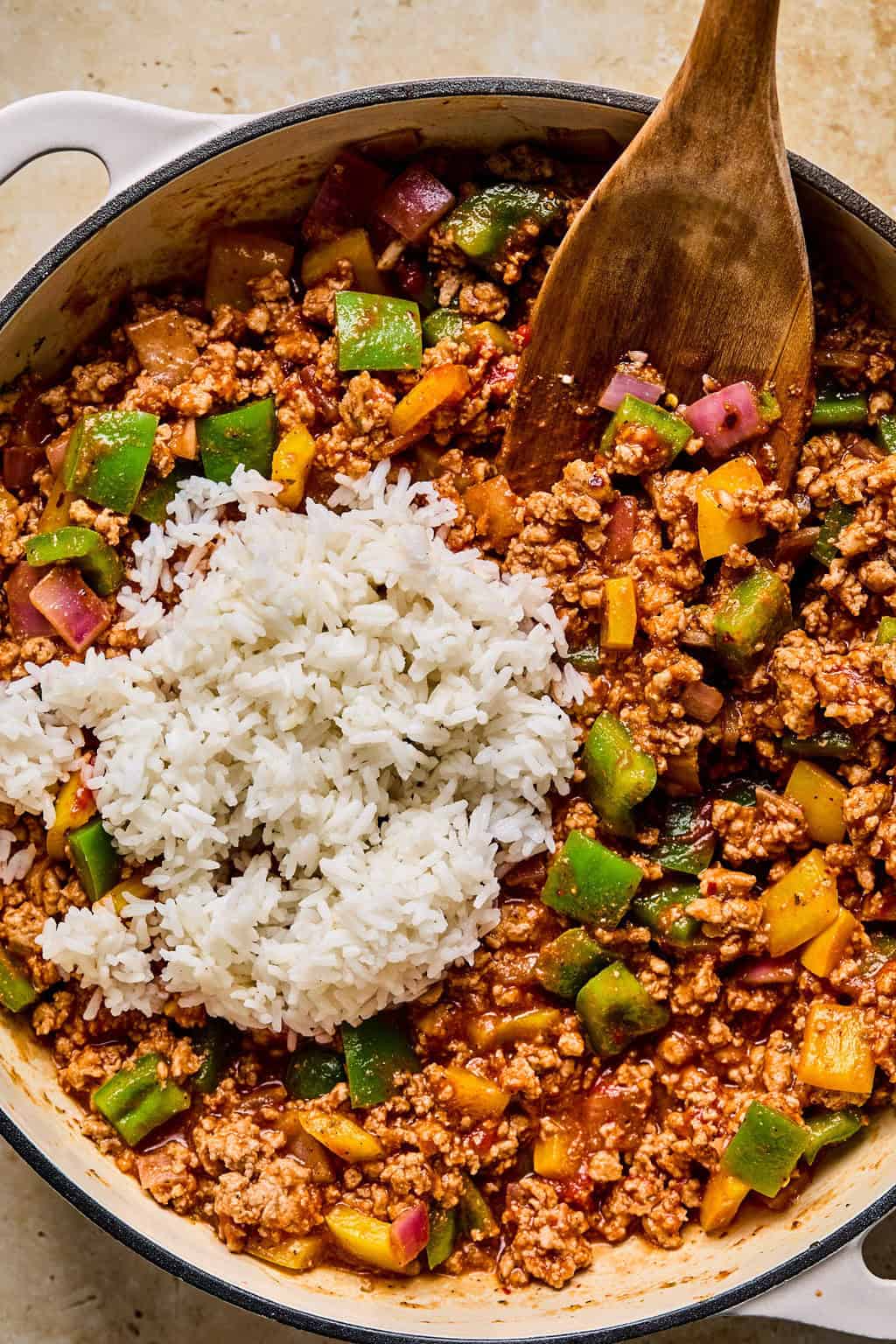 Cooked rice added to simple ground turkey skillet with wooden spoon in pan.