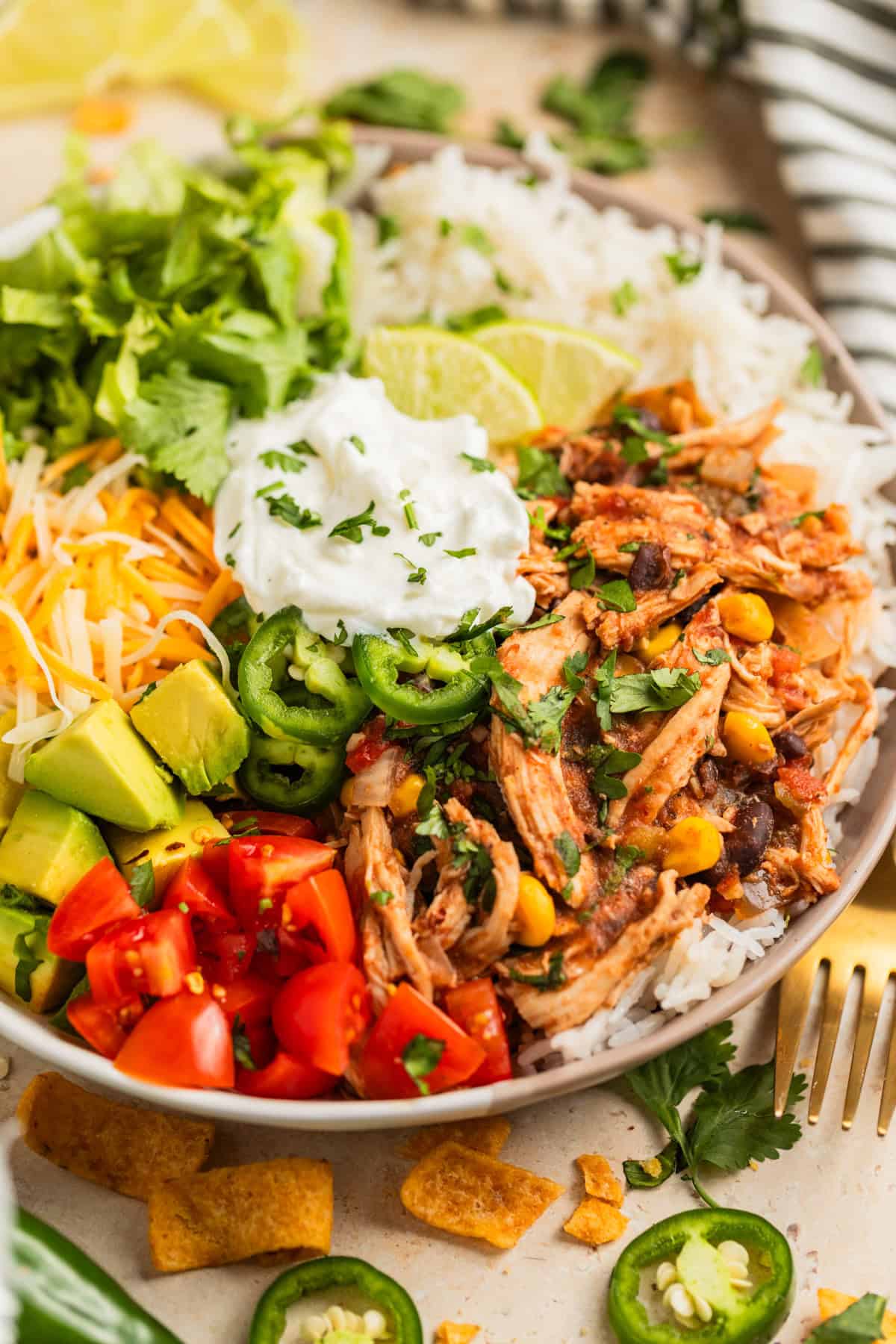 Slow cooker chicken burrito bowl served with rice, limes, cilantro, tomatoes and other ingredients.