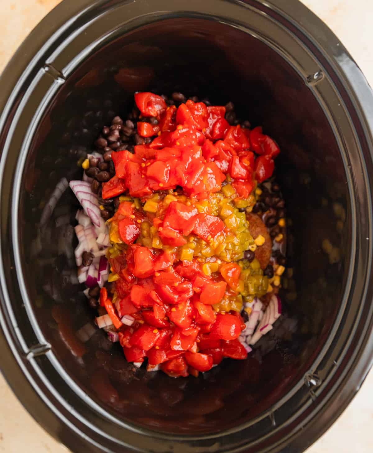 Crockpot with chicken topped with tomatoes, peppers, beans and corn.