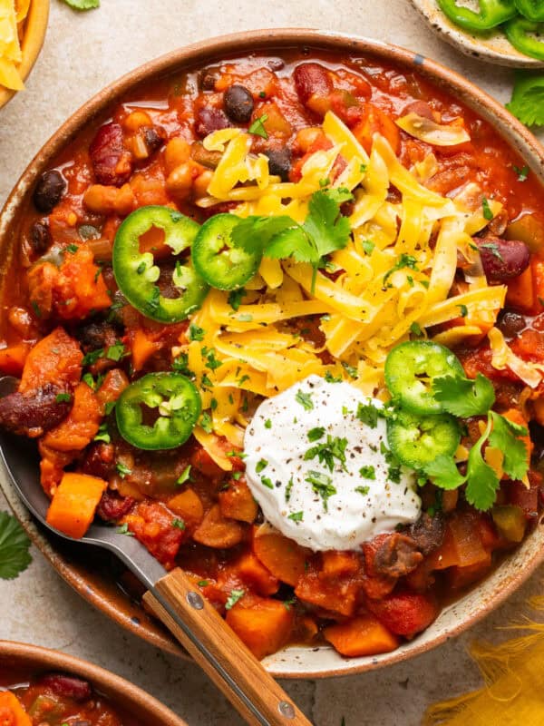 Bowl with vegetarian sweet potato chili with toppings and spoon propped to the side of the bowl.