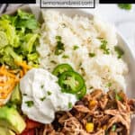 White plate with slow cooker chicken burrito bowls topped with rice, cilantro, cheese, sour cream and more.
