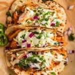 BBQ chicken tacos topped with slaw and chopped cilantro and red onion on parchment.