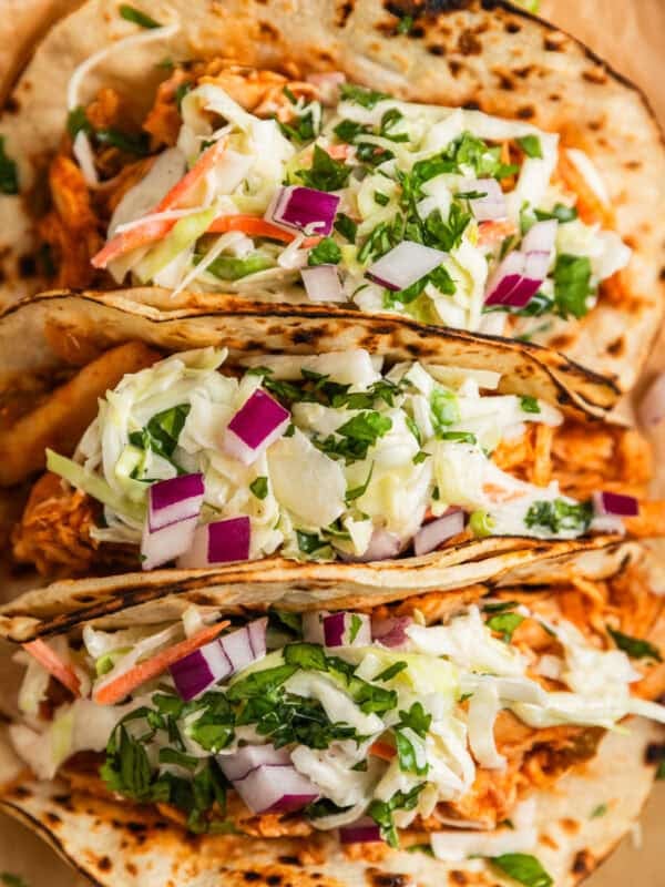 BBQ chicken tacos topped with slaw and chopped cilantro and red onion on parchment.