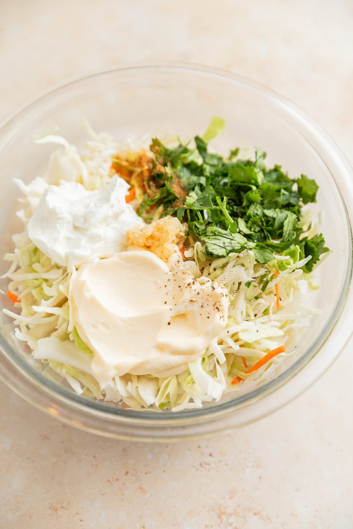 Cabbage, mayo, sour cream, and other ingredients in glass mixing bowl.