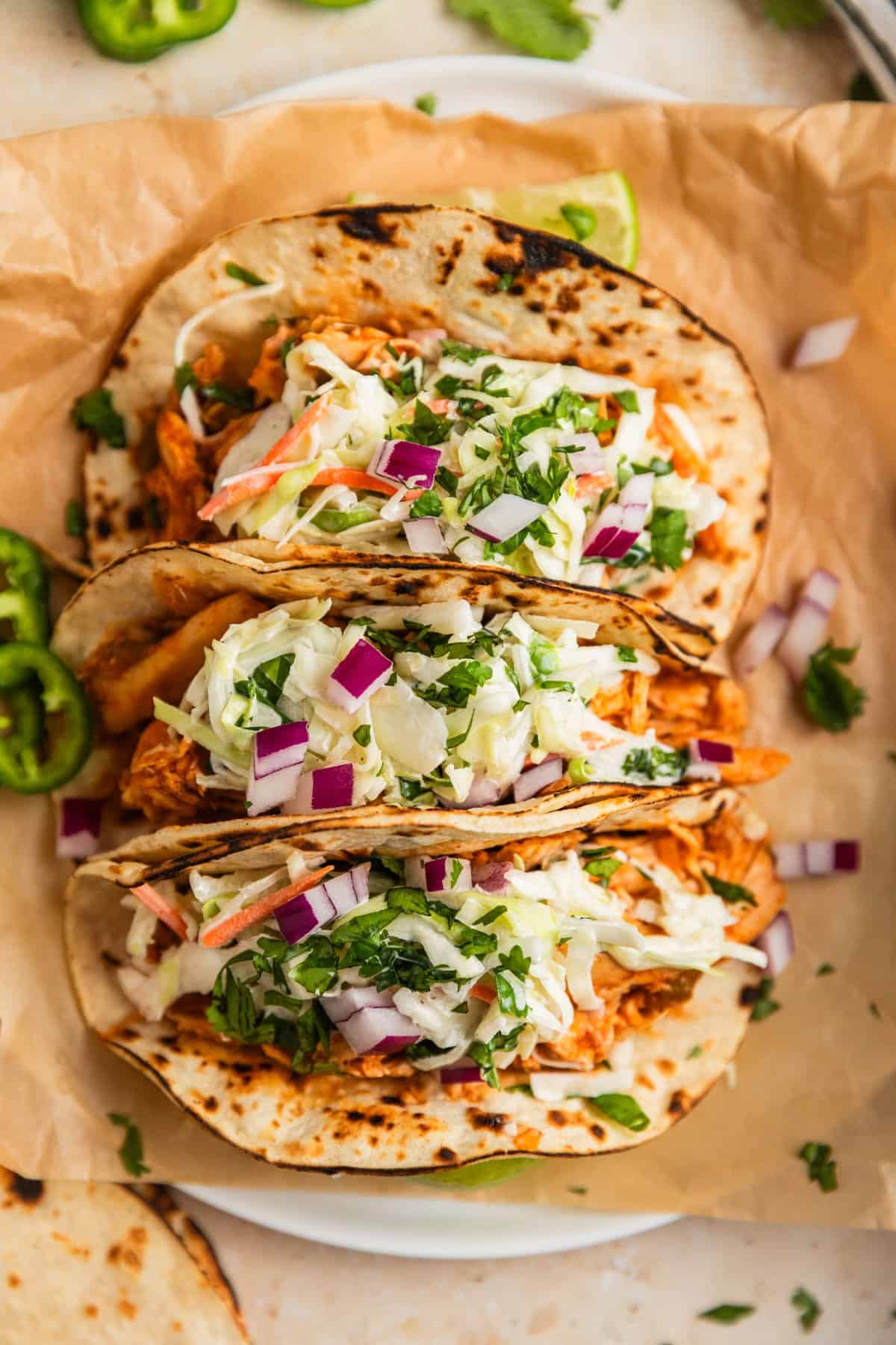 Three chicken tacos on parchment topped with cole slaw.