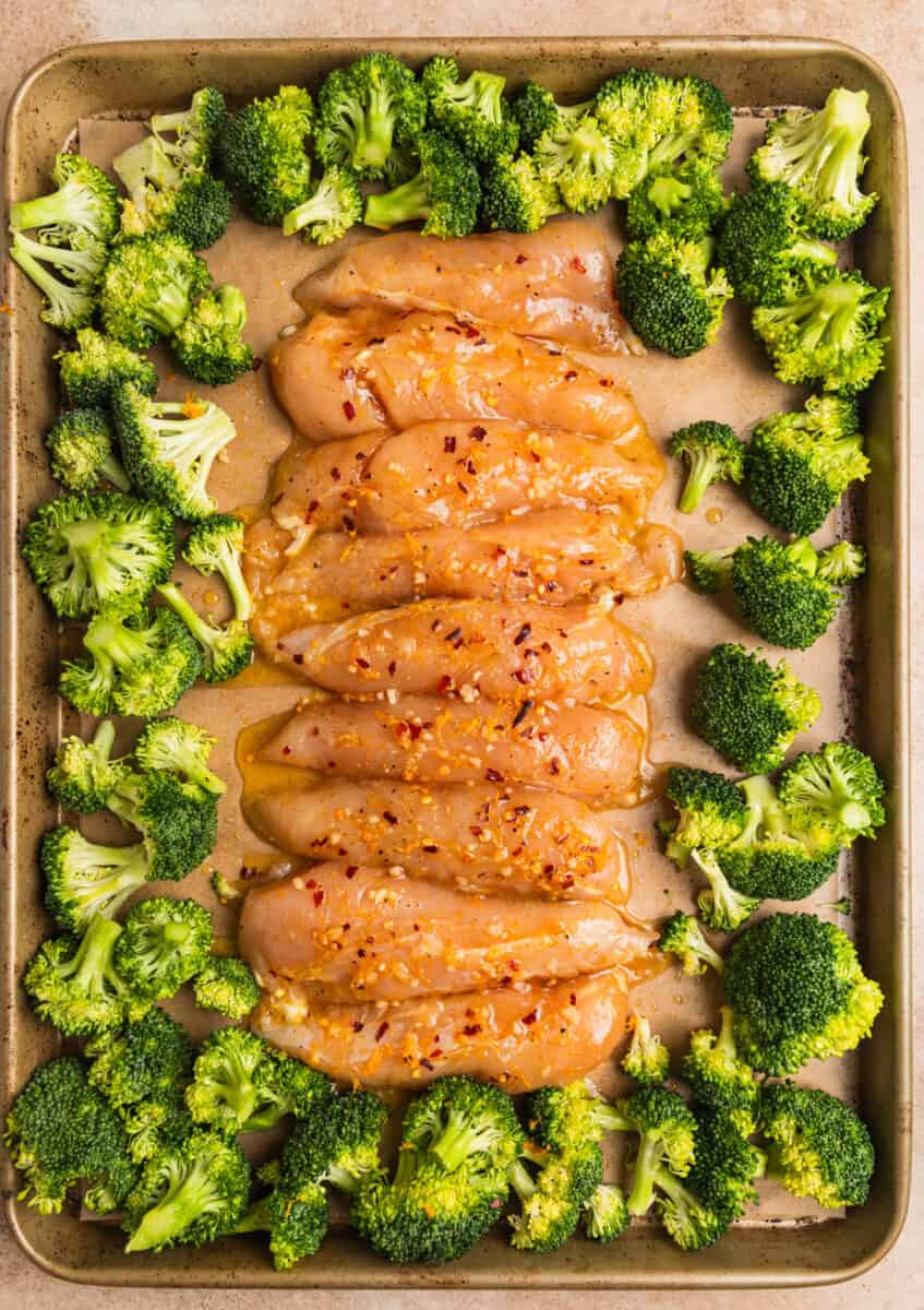 Marinated orange chicken tenderloins and broccoli on sheet pan.