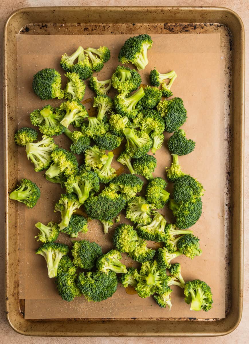 Broccoli on parchment lined baking sheet tossed in olive oil and seasoning.