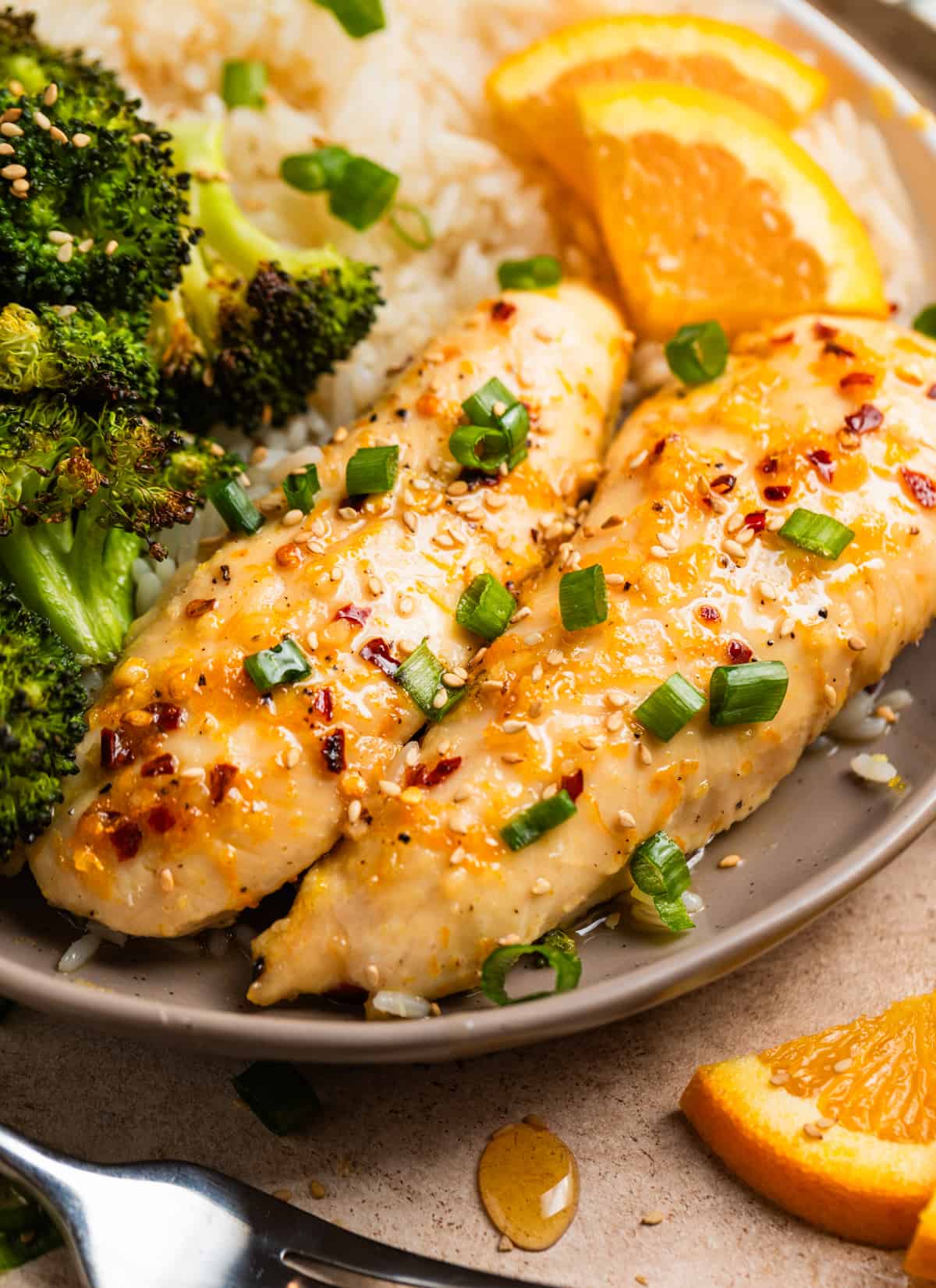 Dish with baked orange chicken, broccoli and rice topped with sliced green onions and sesame seeds.