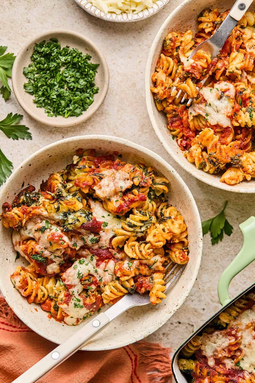 Bowls with baked cottage cheese and spinach pasta with fresh herbs and cheese melted on top.