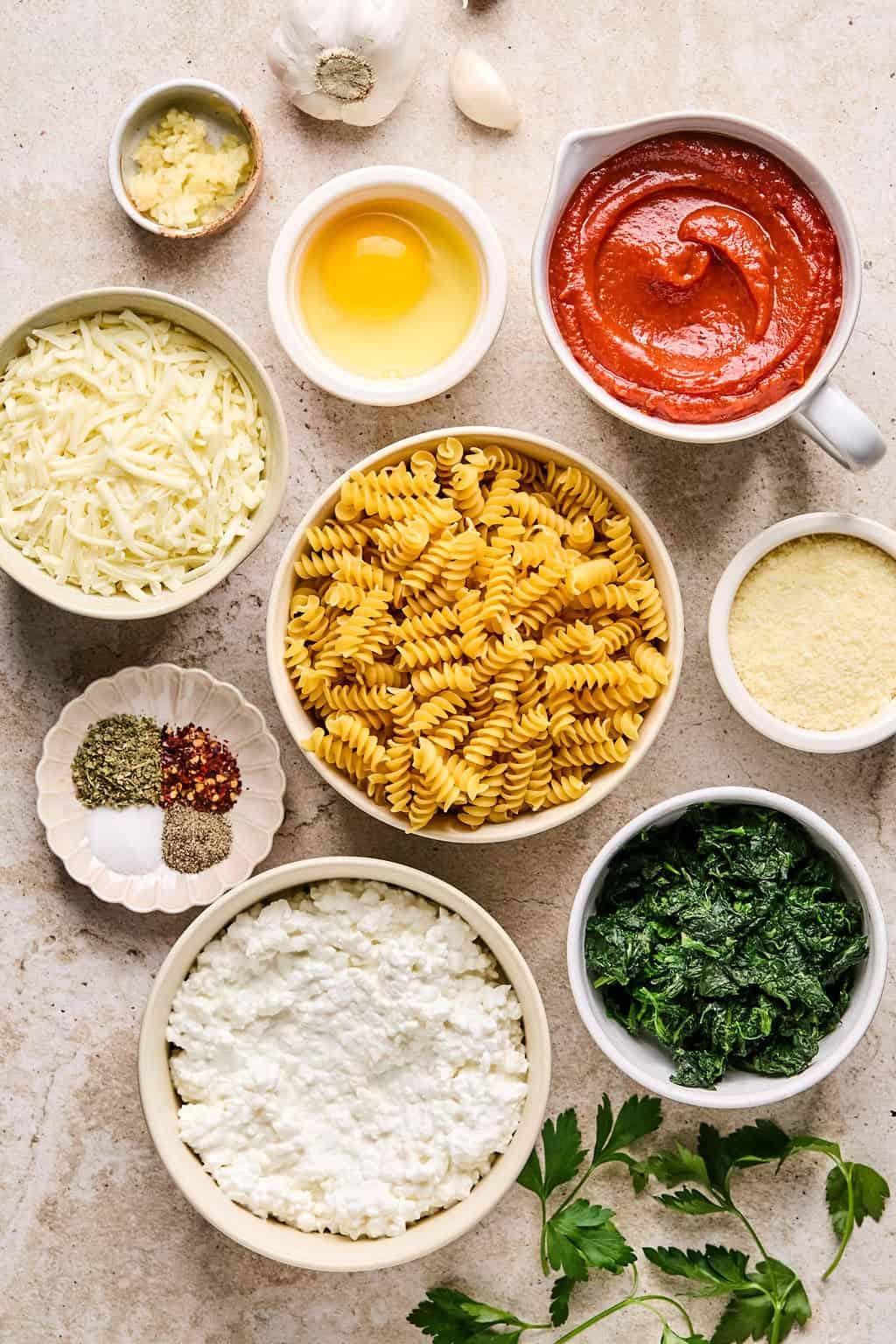 Rotini pasta, spinach, tomato sauce, cottage cheese and other ingredients on surface.