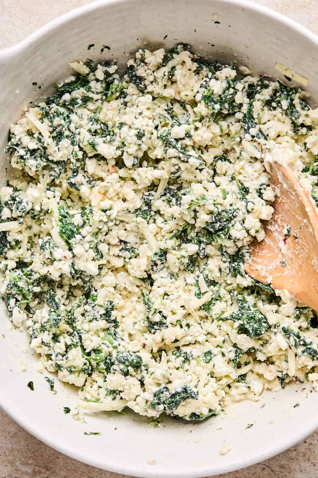 Spinach pasta bake cheese mixture prepped in bowl with spoon.